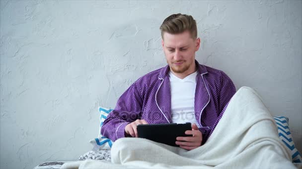 Αρσενικό πελάτη των online αγορών. Άνθρωπος με tablet που κάθεται στο κρεβάτι. - Πλάνα, βίντεο