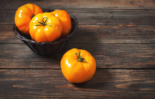 gele tomaten in een rieten mand op houten achtergrond - Foto, afbeelding