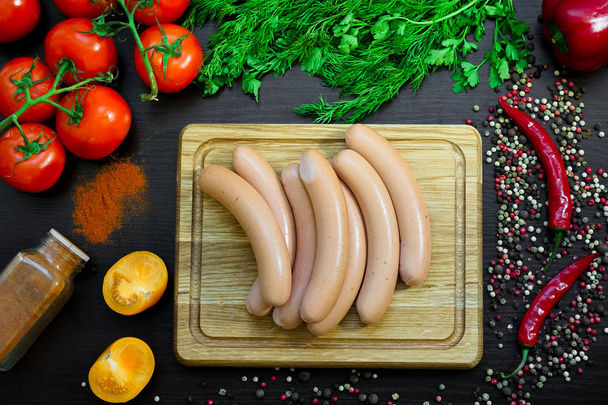 Sausages on cutting board arranged with vegetables - Фото, изображение