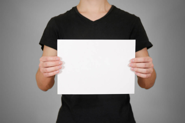 Man in black t shirt holding blank white A4 paper. Leaflet prese - Foto, Imagen