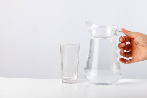 Mão derramando água de jarro de vidro para vidro contra fundo branco
 - Foto, Imagem
