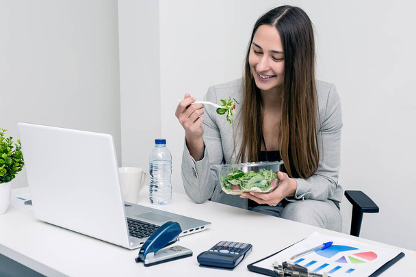 Cheerful woman eating salad in office - Fotó, kép