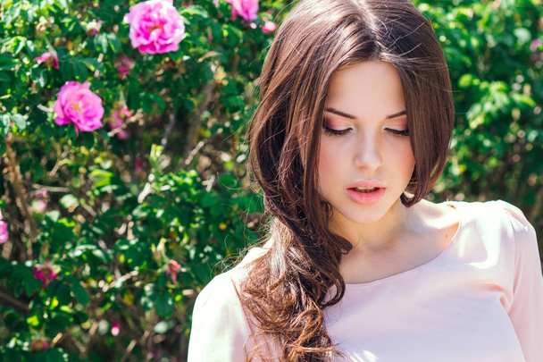 Gyönyörű fiatal nő, hosszú göndör haj pózol egy kert roses közelében. Az a fogalom a reklám parfüm. - Fotó, kép