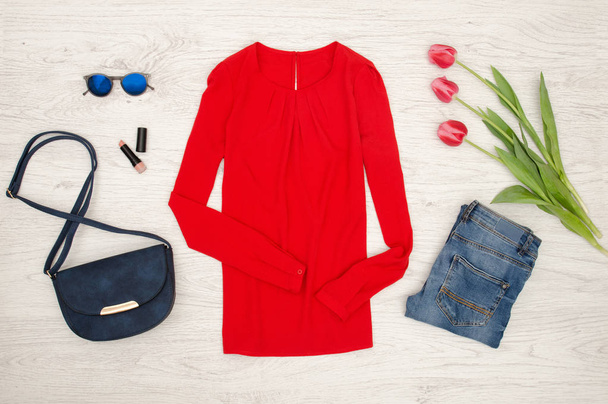 Fashion concept. Red blouse, jeans, handbag, sunglasses, lipstick and pink tulips. Top view, light wood background - Photo, Image