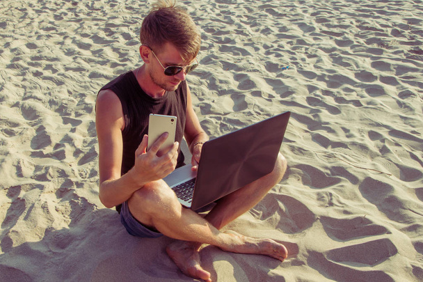 Молодой человек работает за ноутбуком на пляже. Дауншифтинг
  - Фото, изображение