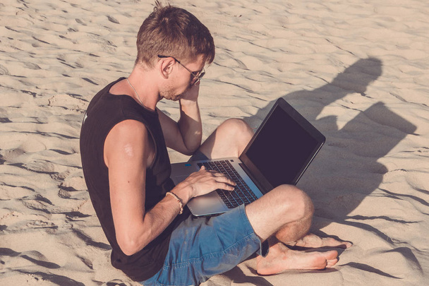 Jeune homme avec ordinateur portable et téléphone portable sur la plage. Oui.
 - Photo, image