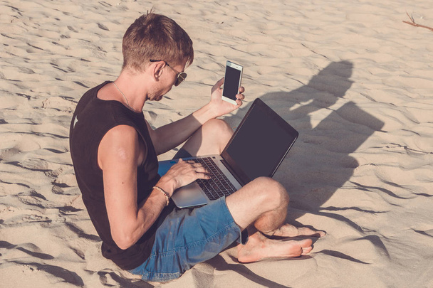 Giovane con computer portatile e telefono cellulare sulla spiaggia. Fa '
 - Foto, immagini