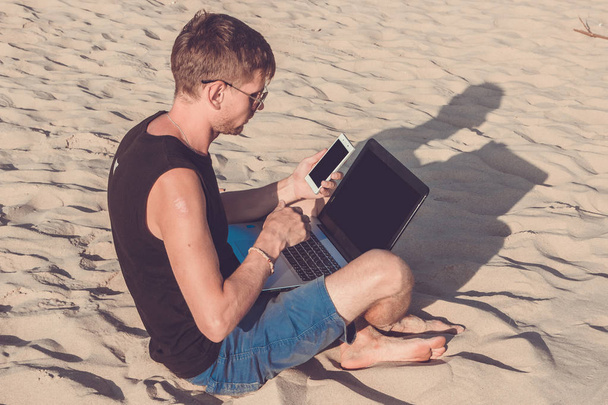 Dizüstü bilgisayar ve cep telefonu sahilde olan genç adam. Yapmak - Fotoğraf, Görsel