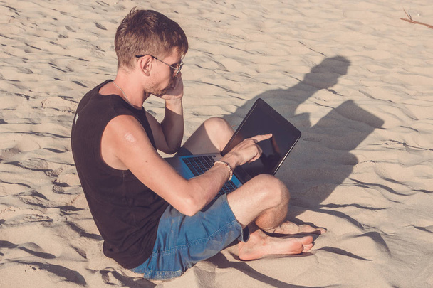 Joven con ordenador portátil y teléfono móvil en la playa. Hazlo.
 - Foto, Imagen