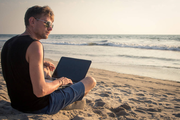 Jonge man werken op laptopcomputer op het strand. Terugschakelen - Foto, afbeelding