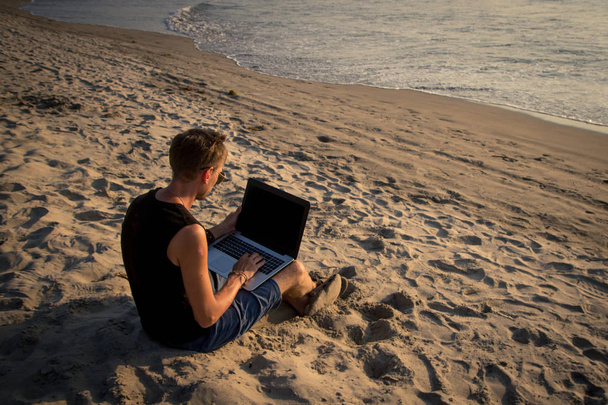 Молодий чоловік працює на портативному комп'ютері на пляжі. Дауншифті
 - Фото, зображення