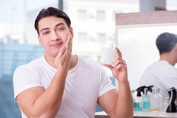 Joven hombre guapo aplicando crema facial - Foto, Imagen
