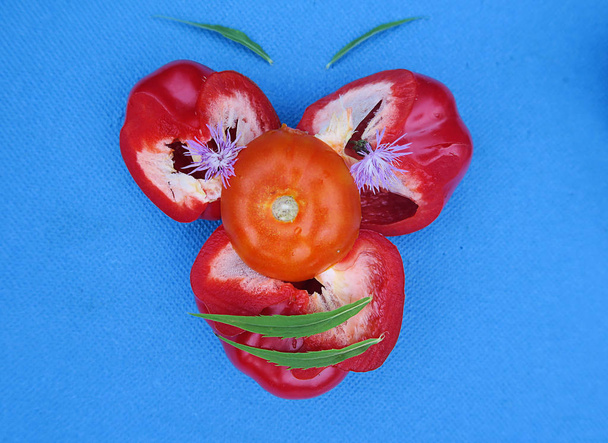 une drôle de nature morte végétale faite de poivrons rouges et d'une tomate rouge sur fond bleu
 - Photo, image
