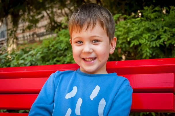 Feliz niño caucásico sonriente sentado en el banco
. - Foto, Imagen