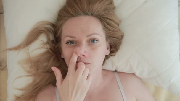 The woman lies on the bed and picks her finger in the nose, close-up. view from above - Imágenes, Vídeo
