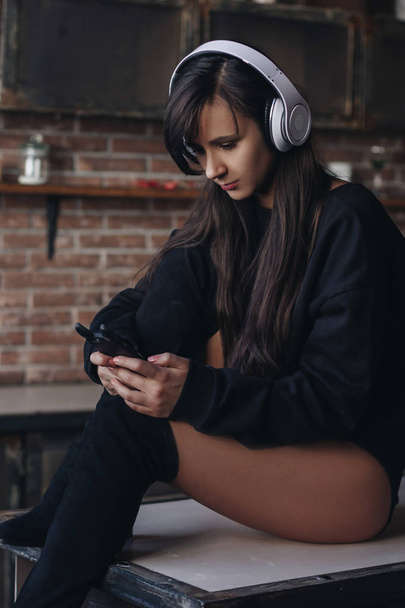 Young woman in headphones sitting on the kitchen table - Foto, Bild