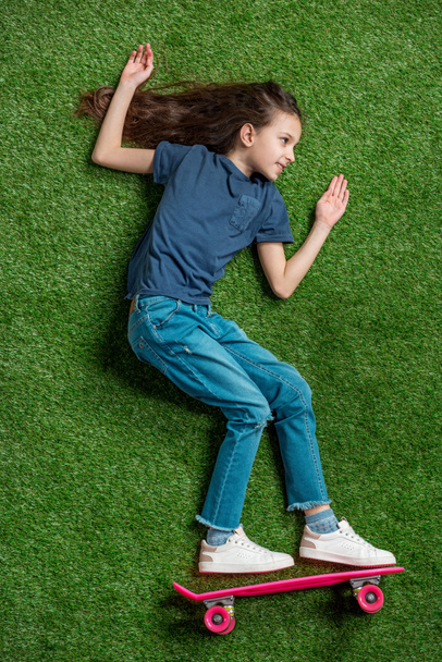 Girl with skateboard lying on grass  - Фото, изображение