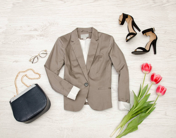 Modekonzept. graue Jacke, Handtasche, Sonnenbrille, Schuhe und rosa Tulpen. Ansicht von oben, heller Holz-Hintergrund - Foto, Bild