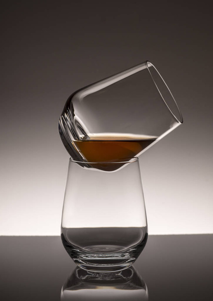 A tower of two transparent glasses with whiskey on a darkening background. - Foto, Imagen