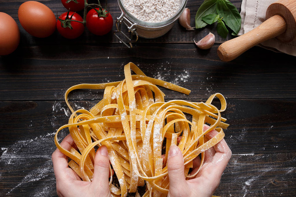 Female hands making fresh homemade pasta. Pasta ingredients on the dark wooden table top view - 写真・画像