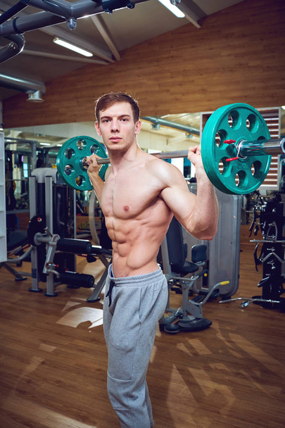 Athlete male doing exercises with a bar lying down in the gym - Фото, изображение