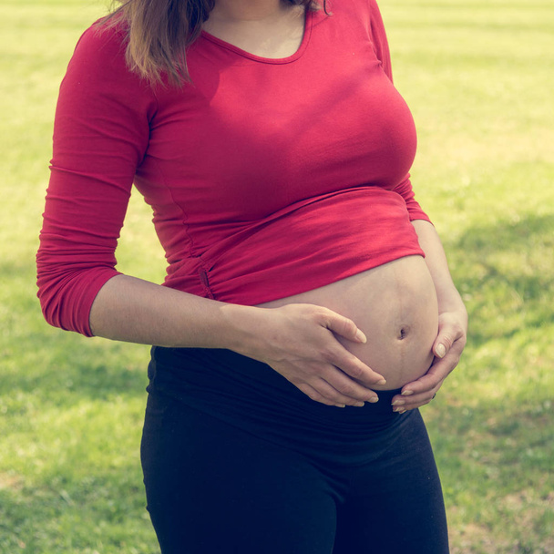 Zwangere vrouw dragen rode shirt zachtjes strelen haar buik. - Foto, afbeelding