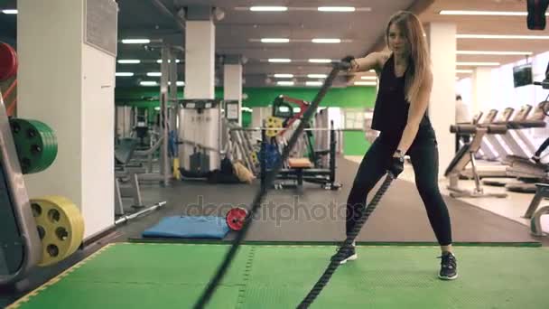 Young attractive woman with battle ropes exercise in the fitness gym and crossfit center - Záběry, video