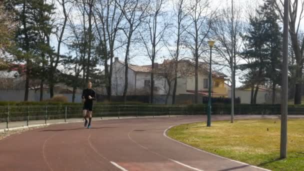 Young athletic man running in the park on the course track - Séquence, vidéo