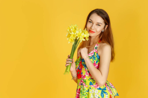 junge Frau mit Blumen in der Hand gegen gelbe Wand - Foto, Bild