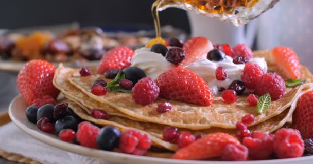 Pouring maple syrup over a breakfast of pancakes with berries, dry fruits and whipped cream - Footage, Video