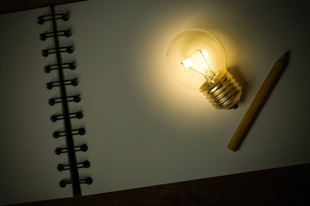 A Light Bulb with a Small Pencil Placed on an Opened Sketchbook - Photo, Image