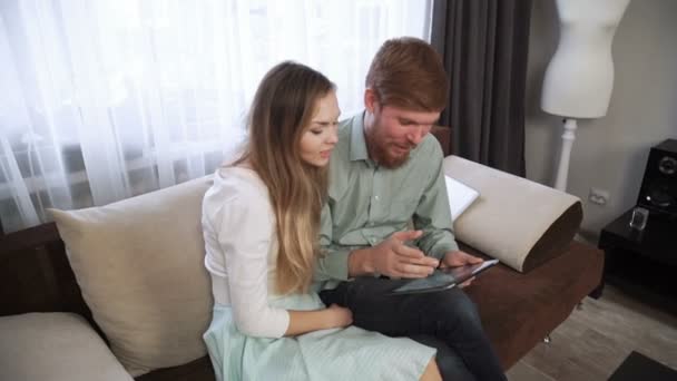 Couple is sitting on the couch sofa at home Look into the tablet and smile, close-up - Video