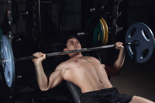 Brutal athletic man pumping up muscles on bench press. - Foto, Bild