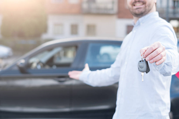 Человек держит ключ от машины рядом со своим автомобилем
  - Фото, изображение