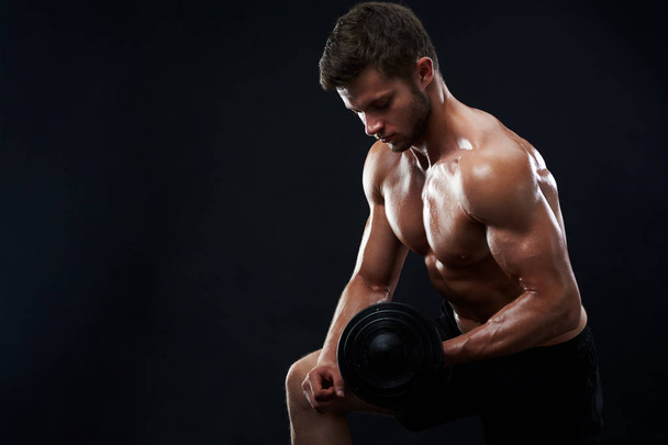 Muscular young man lifting weights on black background - Foto, Imagen