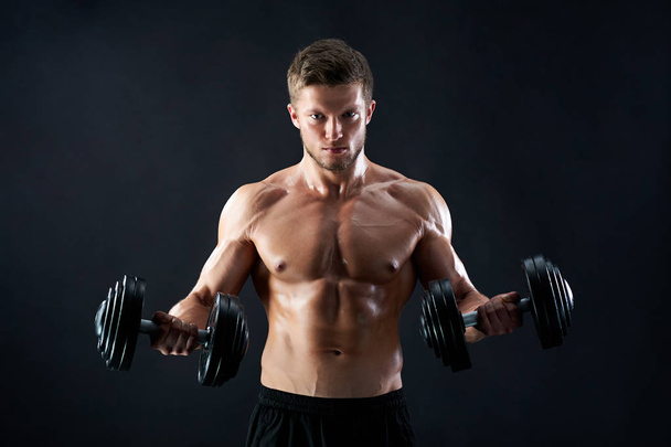 Muscular young man lifting weights on black background - Fotografie, Obrázek