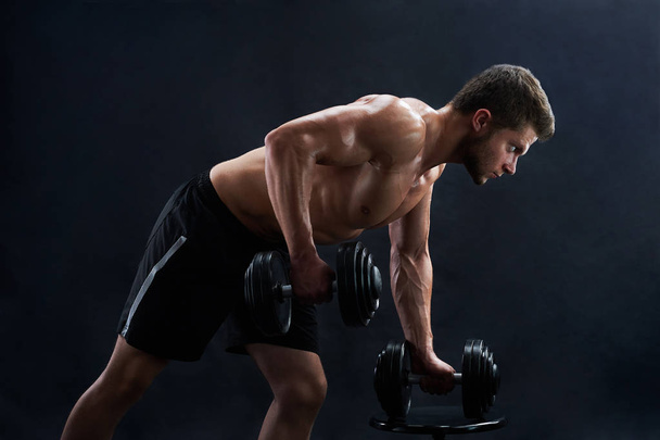 muskulöser junger Mann stemmt Gewichte auf schwarzem Hintergrund - Foto, Bild