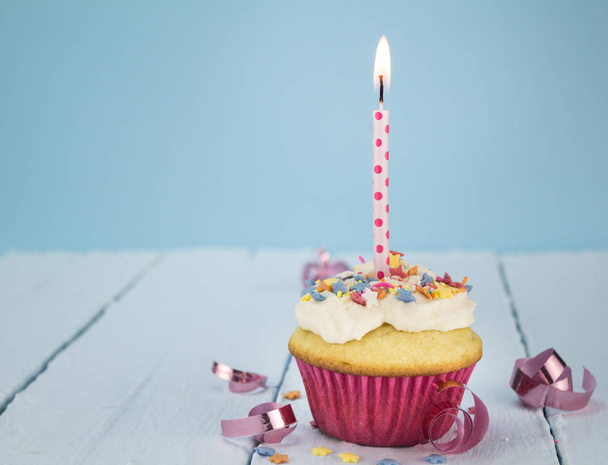 Tasse Kuchen mit einer Kerze auf blauem Hintergrund - Foto, Bild
