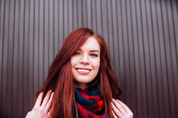 Close up view of attractive happy Caucasian woman with ginger hair wearing stylish clothes looking and smiling at the camera posing against wall. Youth and happiness concept - Foto, imagen