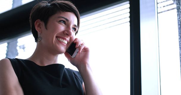 businesswoman speaking on phone beside window of modern office   - Zdjęcie, obraz