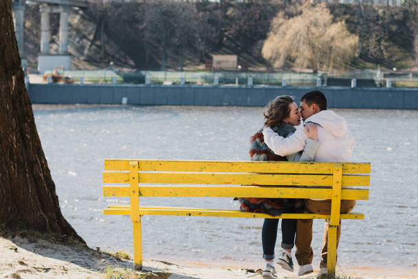Happy couple in love hugging and sharing emotions, holding hands on a bench by the river - Foto, Imagen