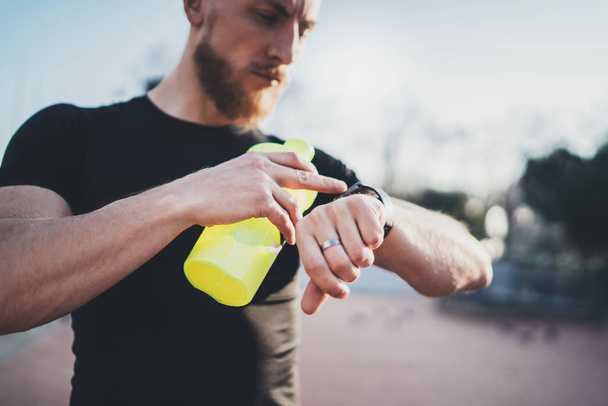 Muscular bearded athlete checking burned calories on electronic smart watch application after good workout outdoor session on city park.Blurred background. - Foto, imagen