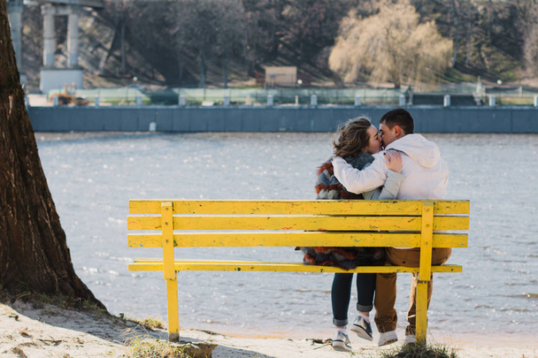 Happy couple in love hugging and sharing emotions, holding hands on a bench by the river - Foto, afbeelding