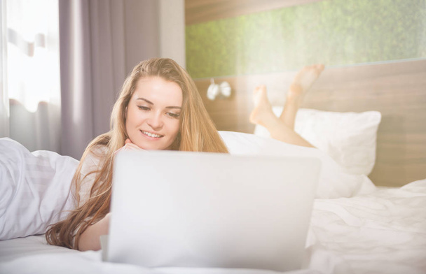 Pretty woman on bed in modern apartment using laptop after wake up - Fotografie, Obrázek