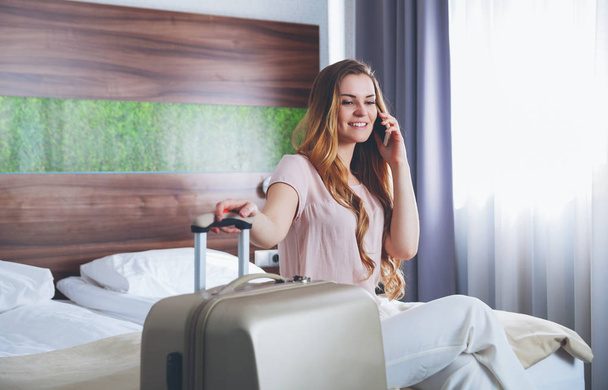 Pretty woman with suitcase in modern hotel apartment using phone - Foto, Bild
