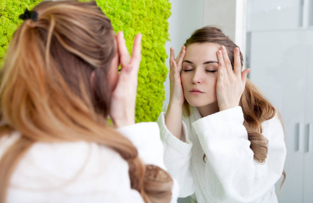 Pretty woman looking at mirror in modern bathroom and aplying cream on face - Фото, зображення