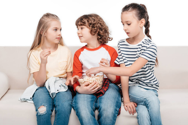 Lindos niños en el sofá con palomitas de maíz
 - Foto, Imagen
