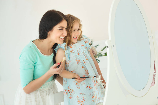 Kleine Tochter und Mutter schminken sich im hellen Raum - Foto, Bild