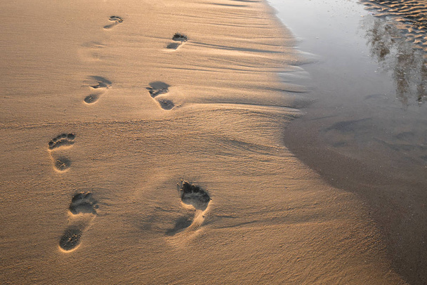 Nyomában a homok a naplemente. Gyönyörű homokos trópusi tengerparton, a lábnyomokat a parton. - Fotó, kép