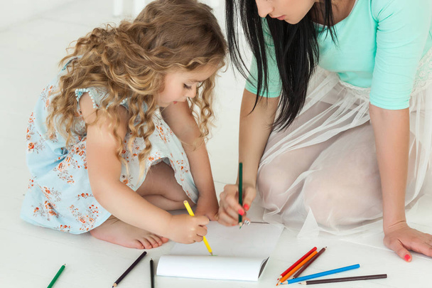 Little cute daughter and her mother drawing with colorful pencil - Foto, Imagen